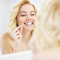 A picture of a young happy woman using dental floss in the bathroom