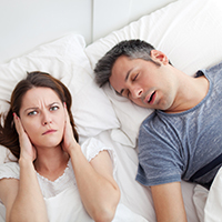 Woman covering ears, annoyed by the snoring of her husband