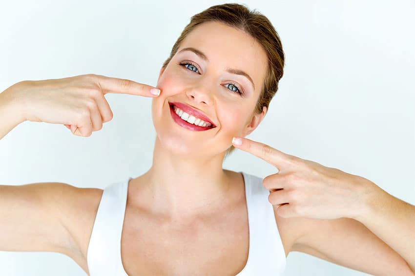 Ten-Easy-Ways-to-Have-Healthy-Teeth-1 Beautiful woman points to her amazing healthy, smile