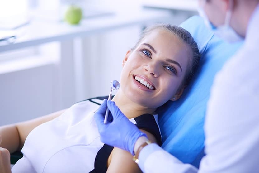 Young Female patient with pretty smile examining dental inspection at dentist office. We talk about holistic dentistry all the time, but what does it mean? And how does holistic dentistry, rather than traditional dentistry, benefit you as the patient?