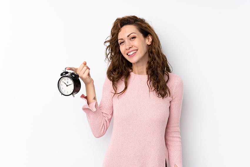 Attractive woman holds up a vintage clock and shows off her smile